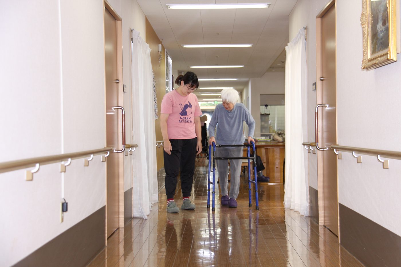 歩行器で廊下を歩く入居者とスタッフ