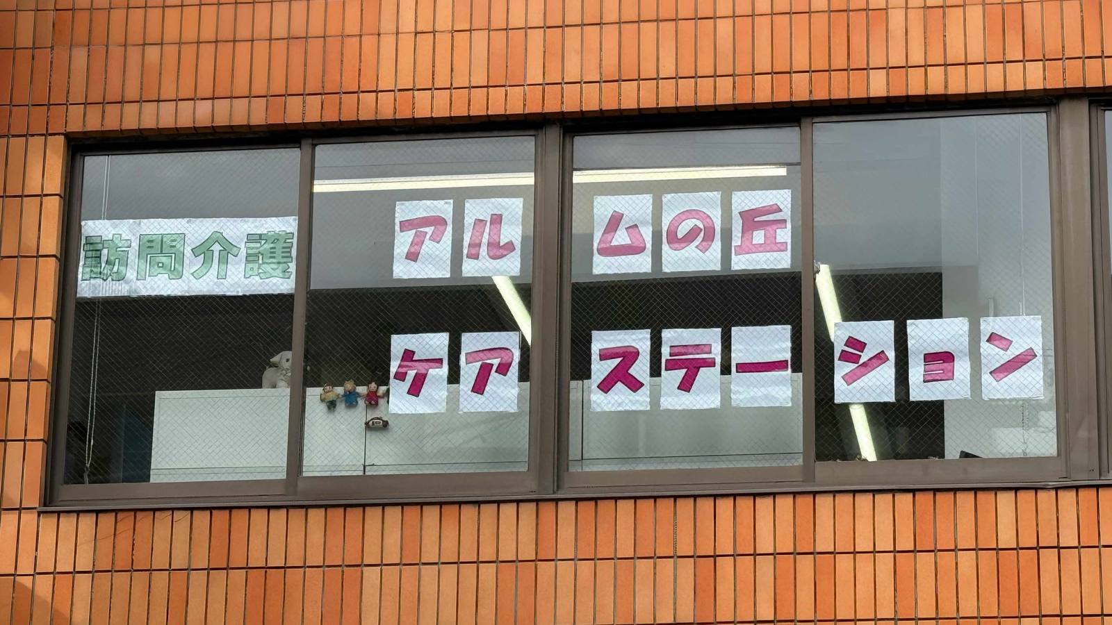 事業所の窓に掲げられた「訪問介護 アルムの丘ケアステーション」の表示